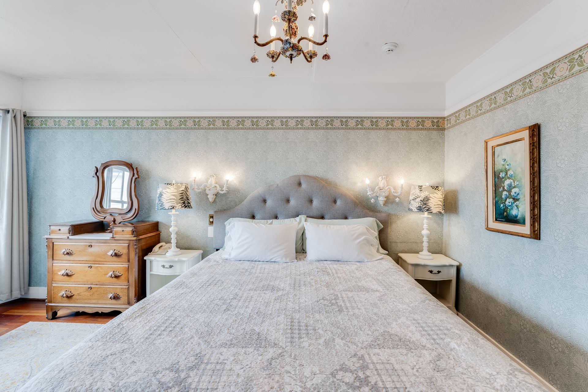 Bedroom with bed, dresser, nightstands, floral wallpaper, and chandelier.