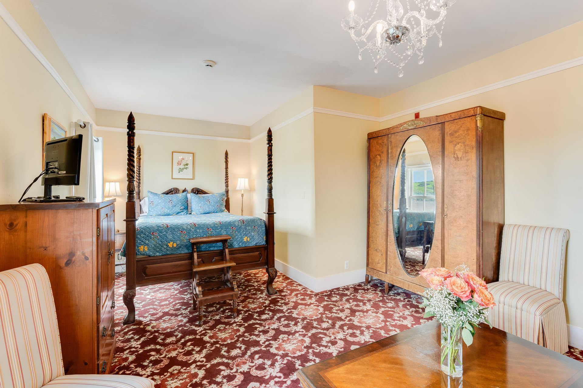 Bedroom with four-poster bed, wooden wardrobe, and floral carpet.