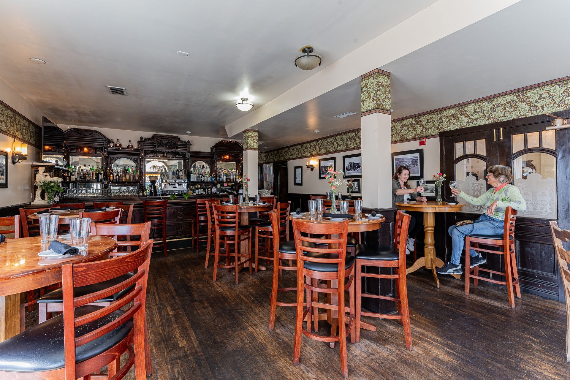 Interior view of a pub with tables, chairs, and a bar; a person sits at a table.