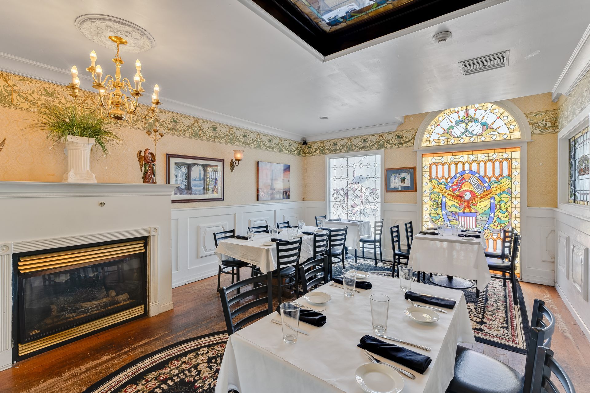 Elegant restaurant dining room with tables set for service, fireplace, and stained glass window.