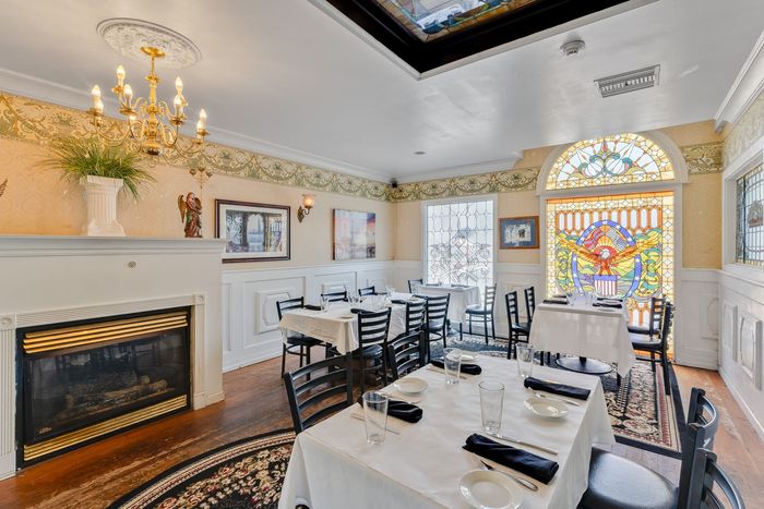 Elegant restaurant dining room with tables set for service, fireplace, and stained glass window.