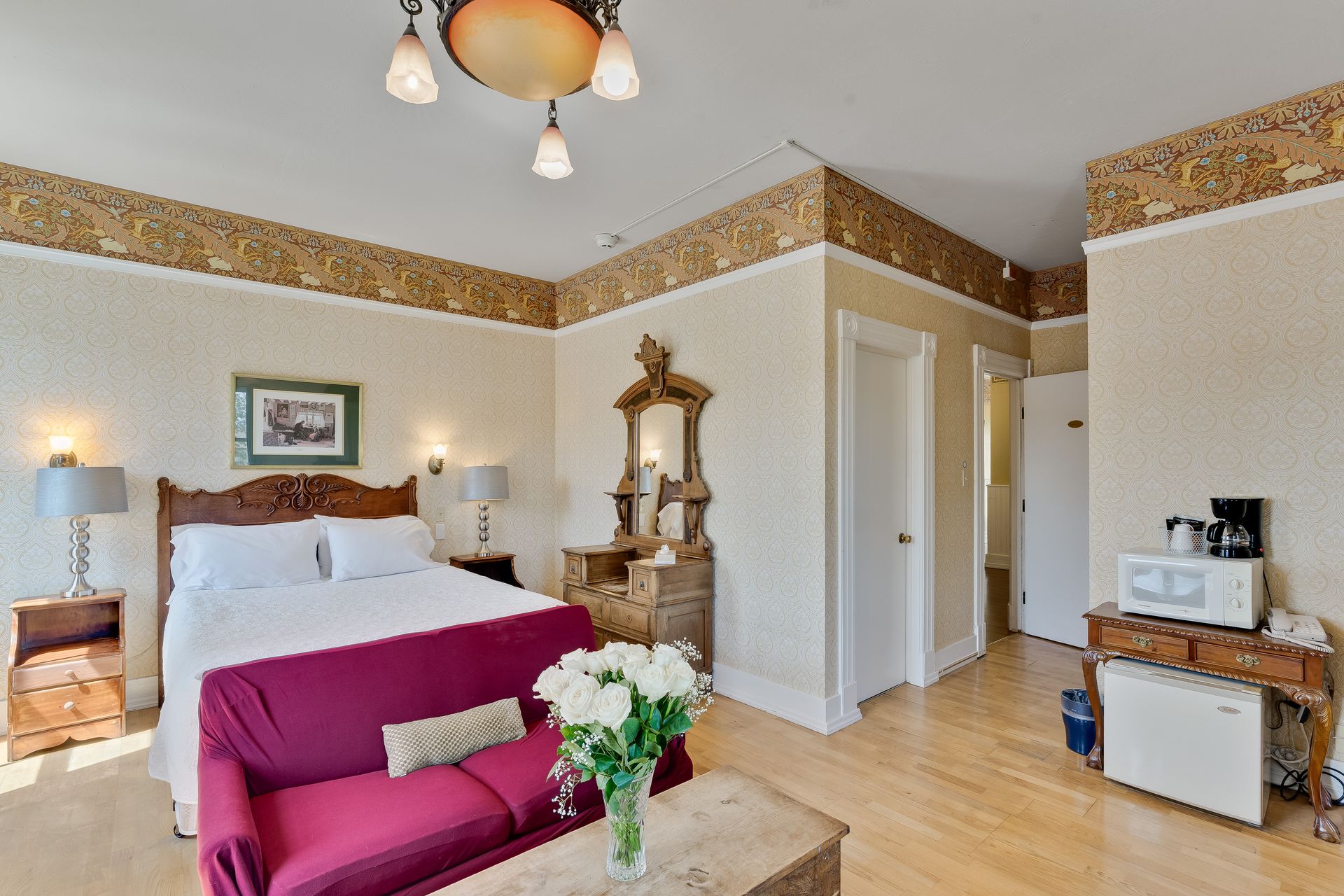 Bedroom with bed, red couch, vanity, microwave, and wood floors.