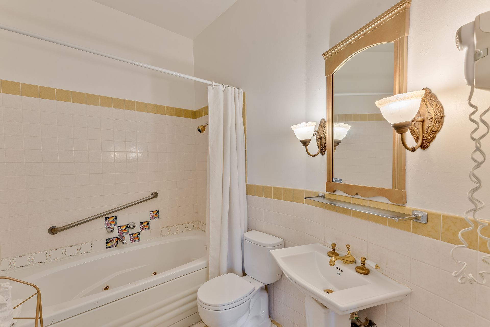 Bathroom with a white tub, toilet, and sink. Gold trim and accents.