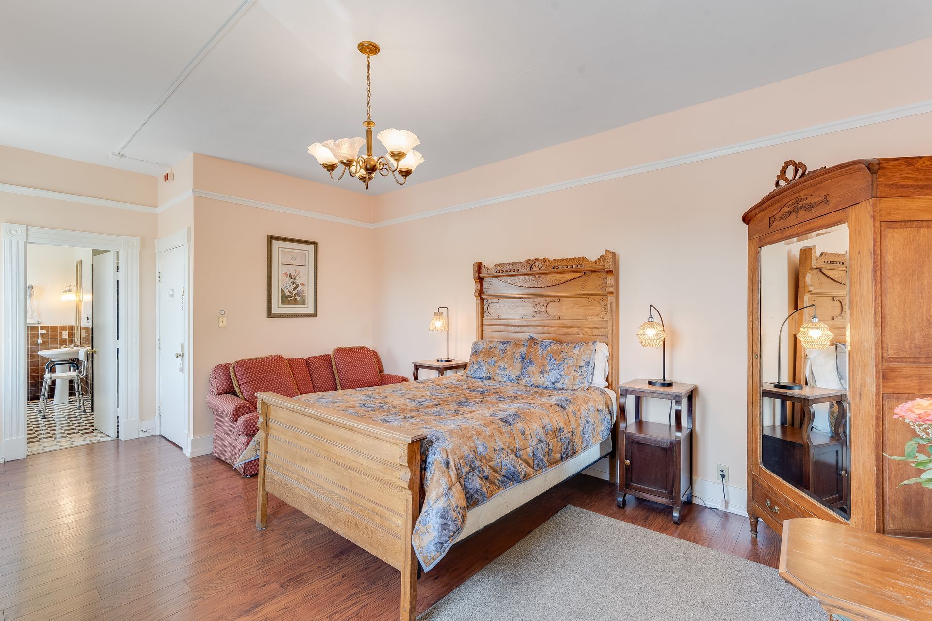 Bedroom with wooden furniture, including a bed, wardrobe, and nightstands, plus a couch and chandelier.
