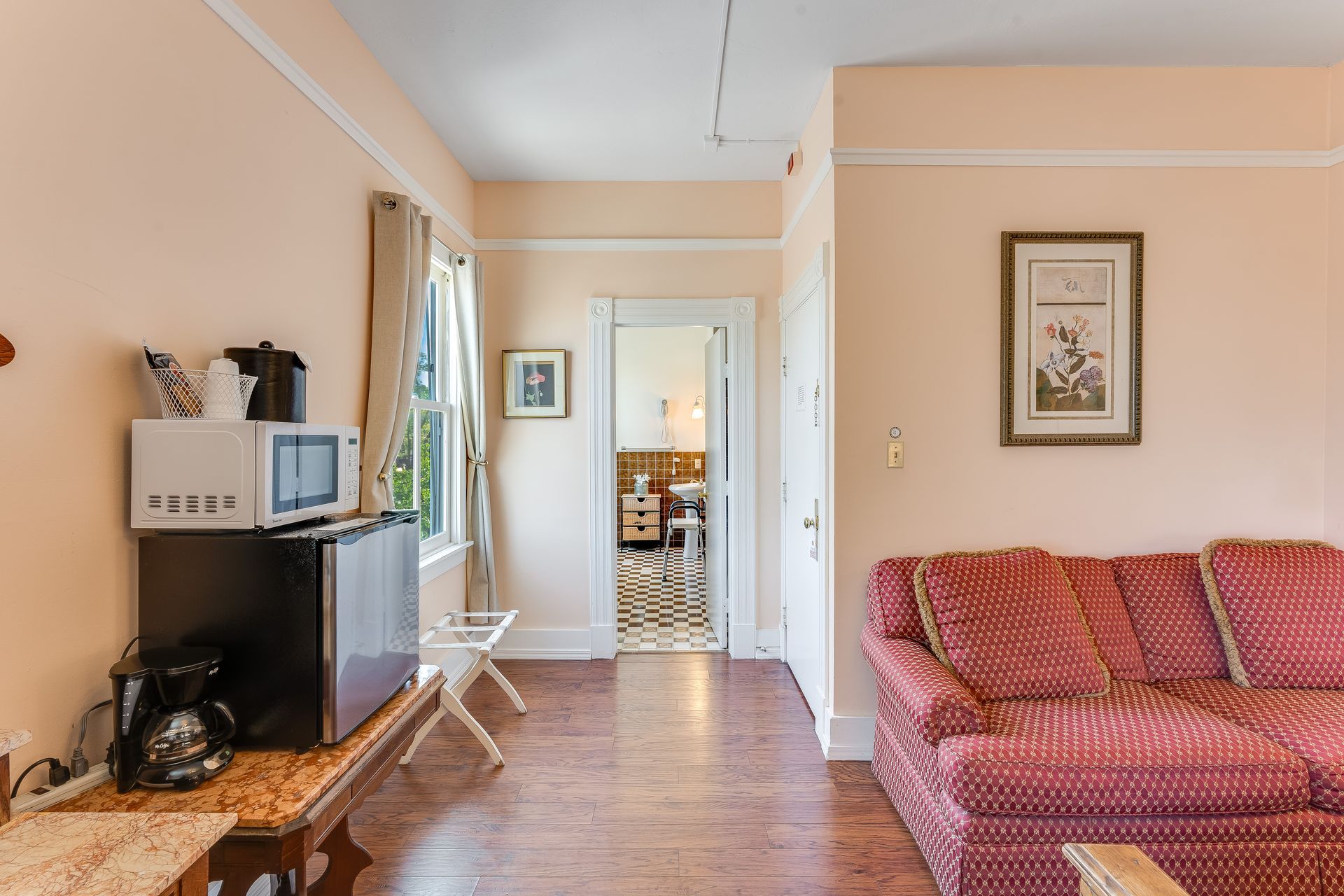 A small living area with pink walls, a red sofa, and a doorway to a kitchen.