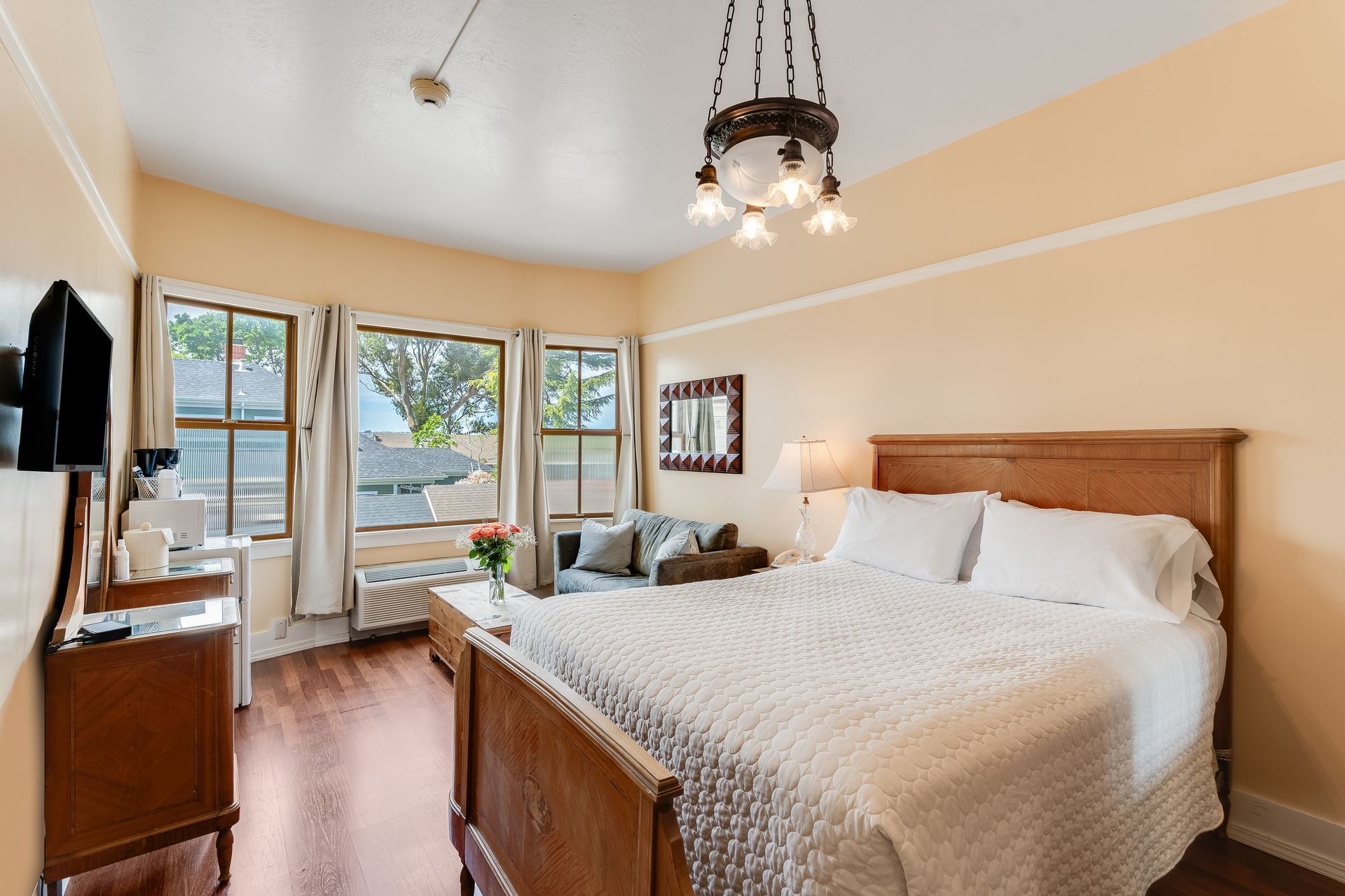 Bedroom with a large bed, windows, and small seating area; warm colors.