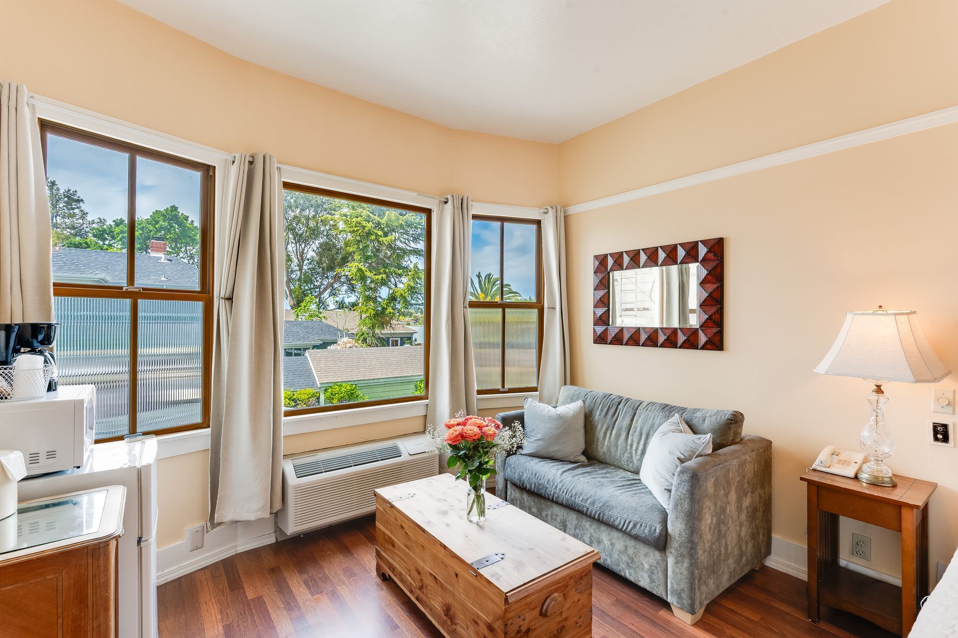 Cozy hotel room with three large windows, sofa, coffee table, and side table with lamp.