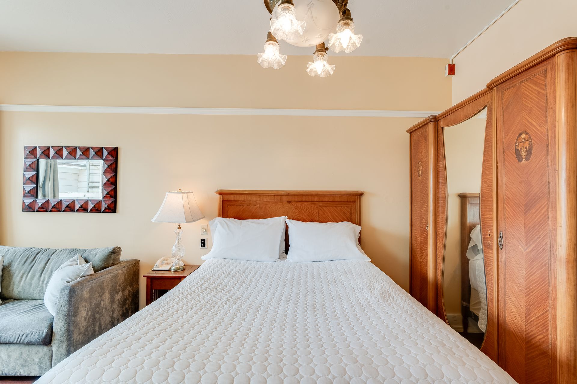 Bedroom with bed, sofa, antique armoire, lamps, and decorative ceiling light.