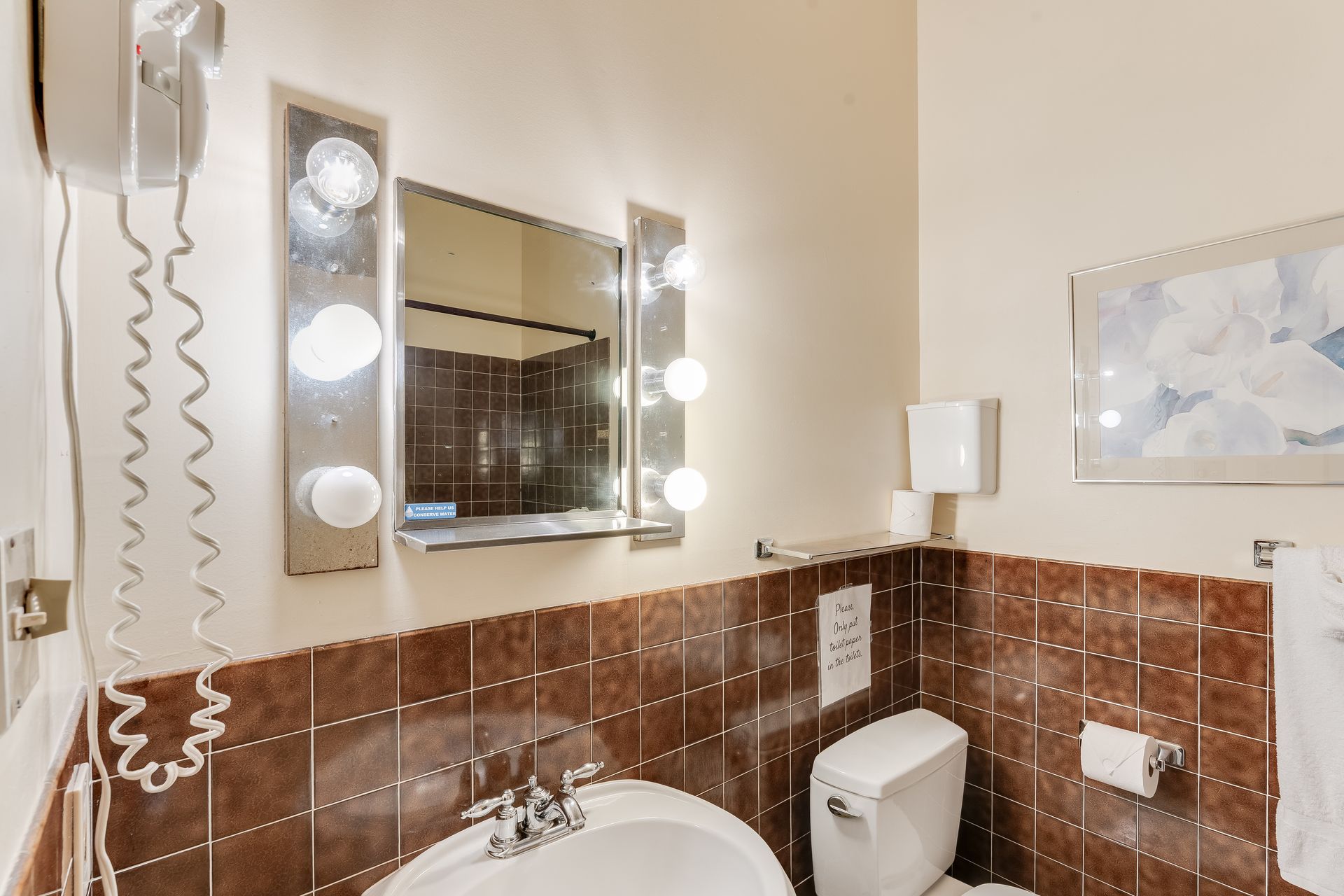 Bathroom with brown tile, a mirror with lights, and a toilet.