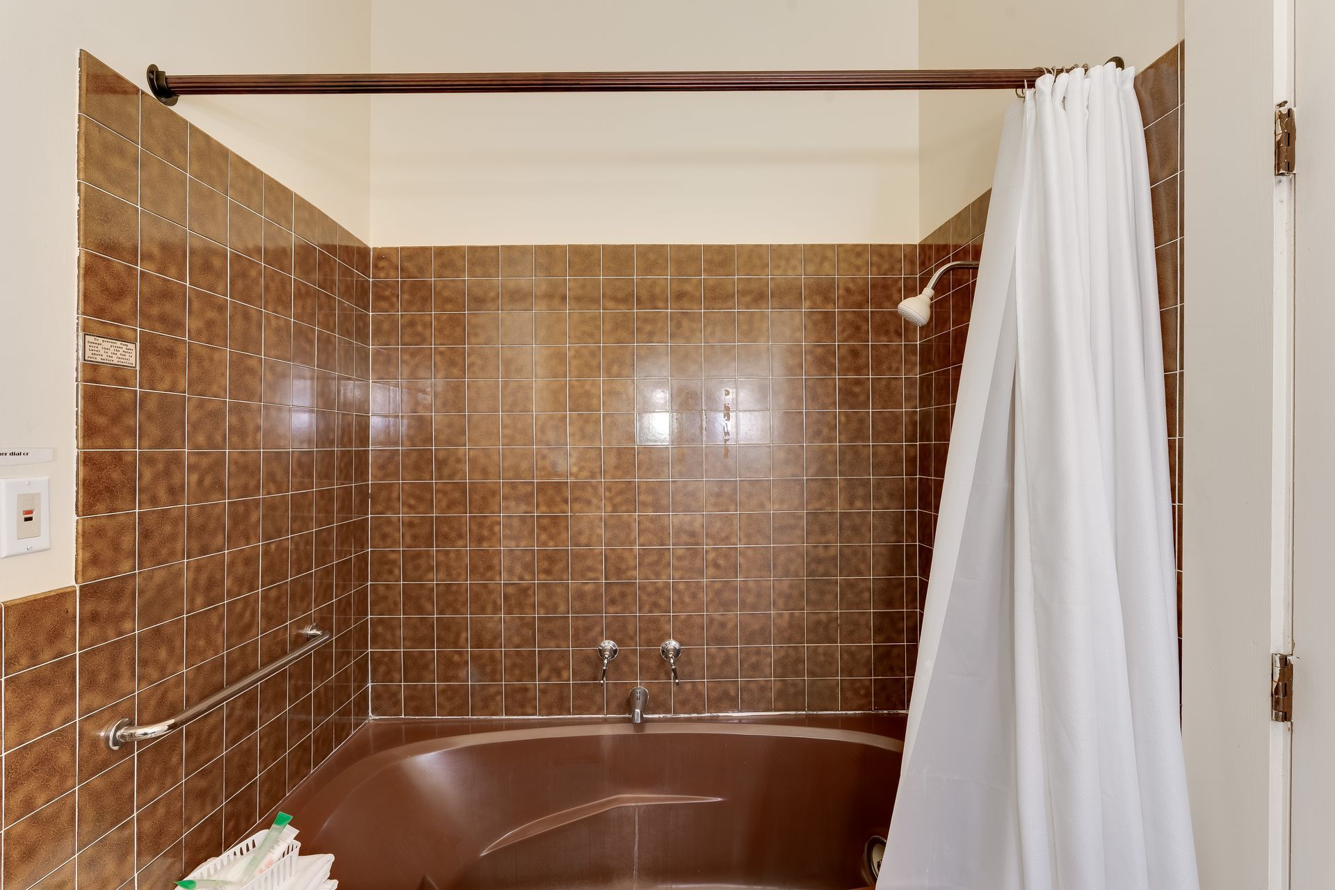 Brown tiled shower stall with a curtain pulled closed.