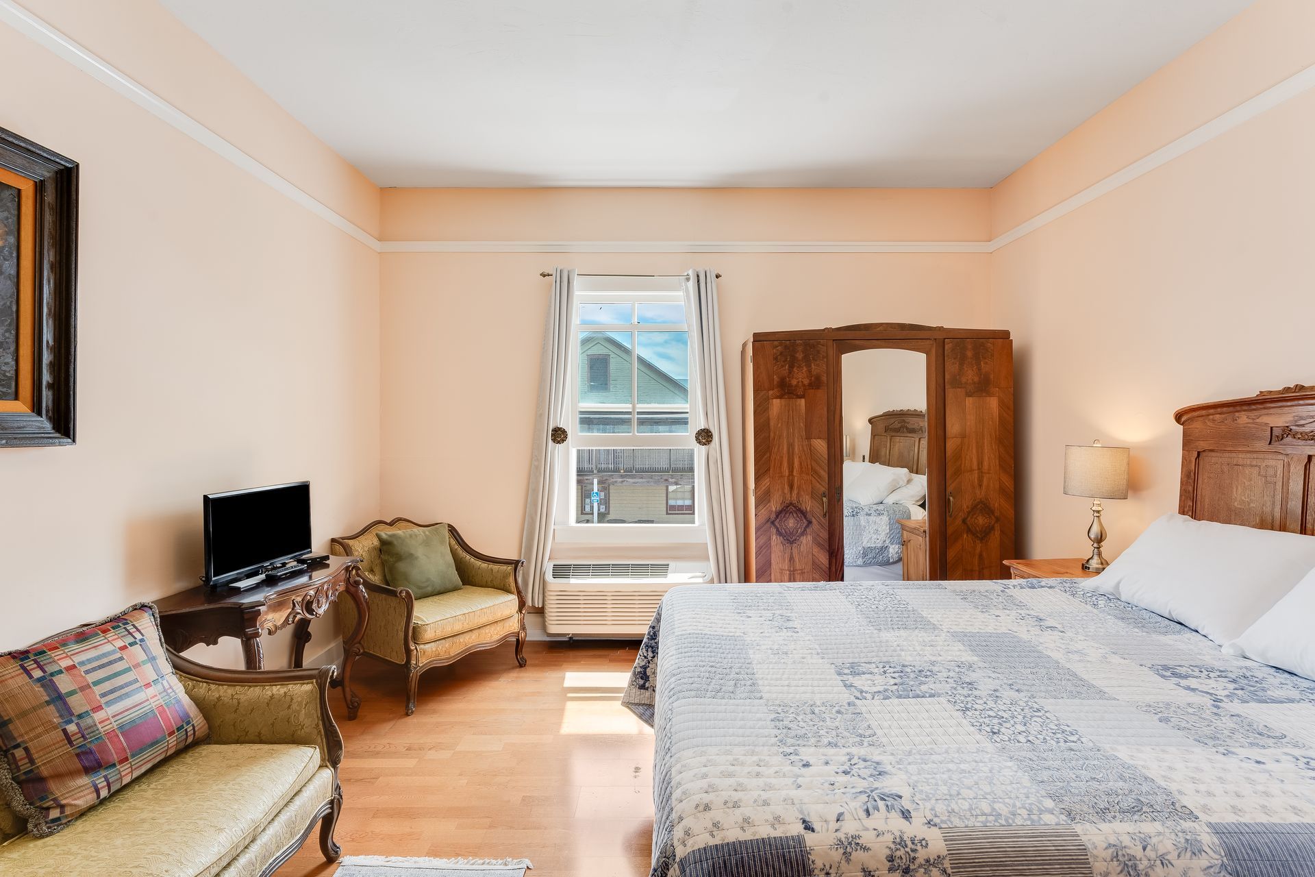Bedroom with a large wooden bed, patterned quilt, armoire, and a small sofa.