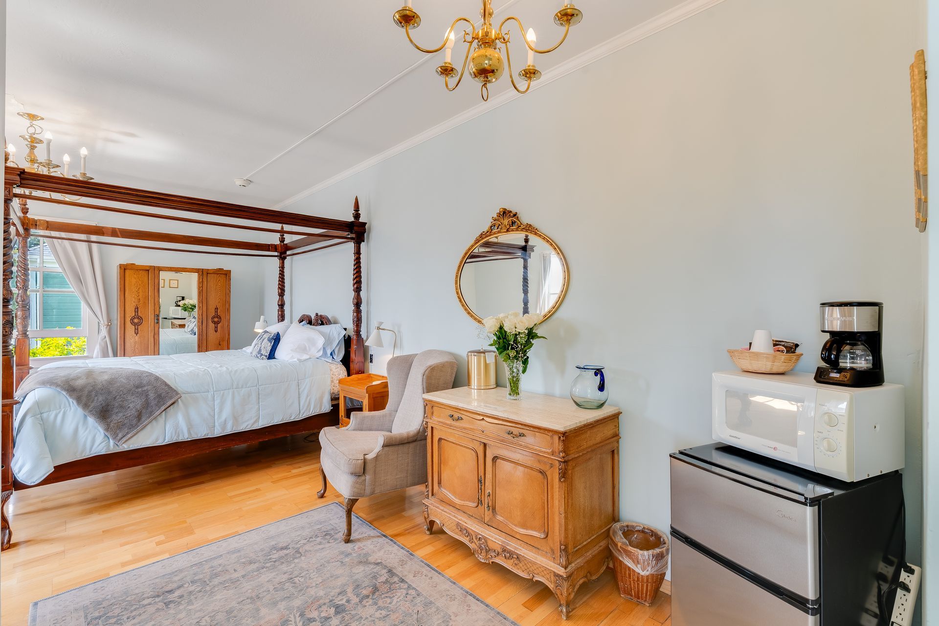 Bedroom with four-poster bed, antique dresser, small fridge, microwave, and chandelier.