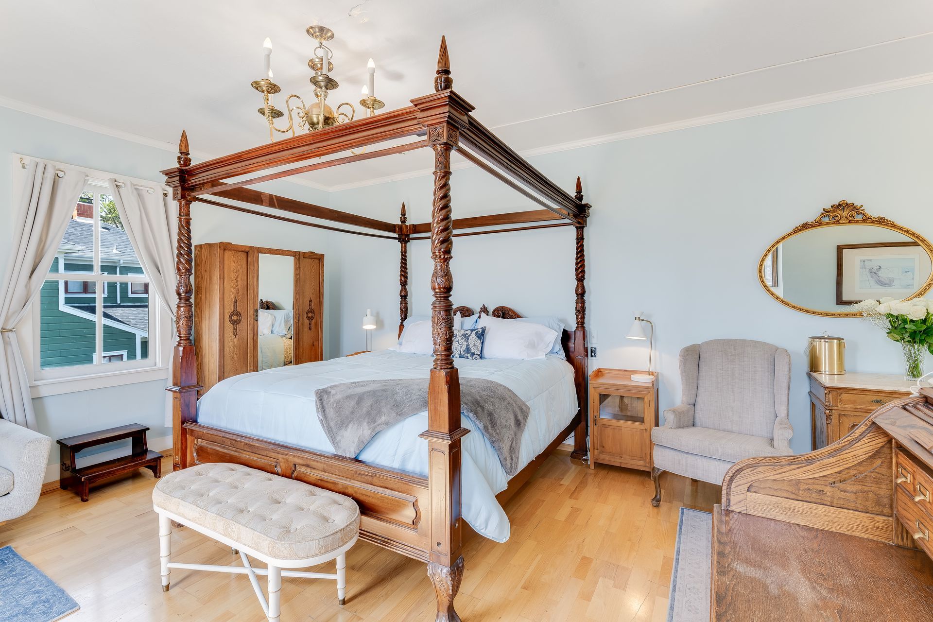 Bedroom with four-poster bed, pale blue walls, hardwood floors, and antique furniture.