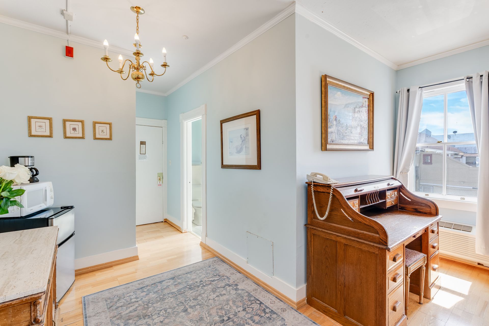 Hallway with desk, framed art, and chandelier; light blue walls, wooden floors.