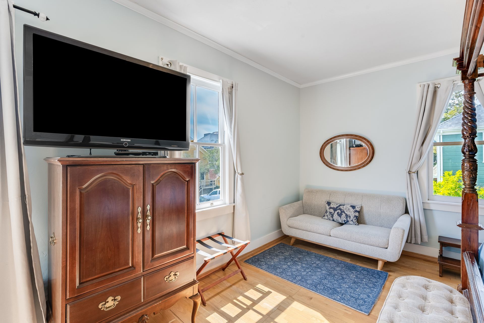 Bedroom with a large TV above a wooden cabinet, sofa, rug, and windows.