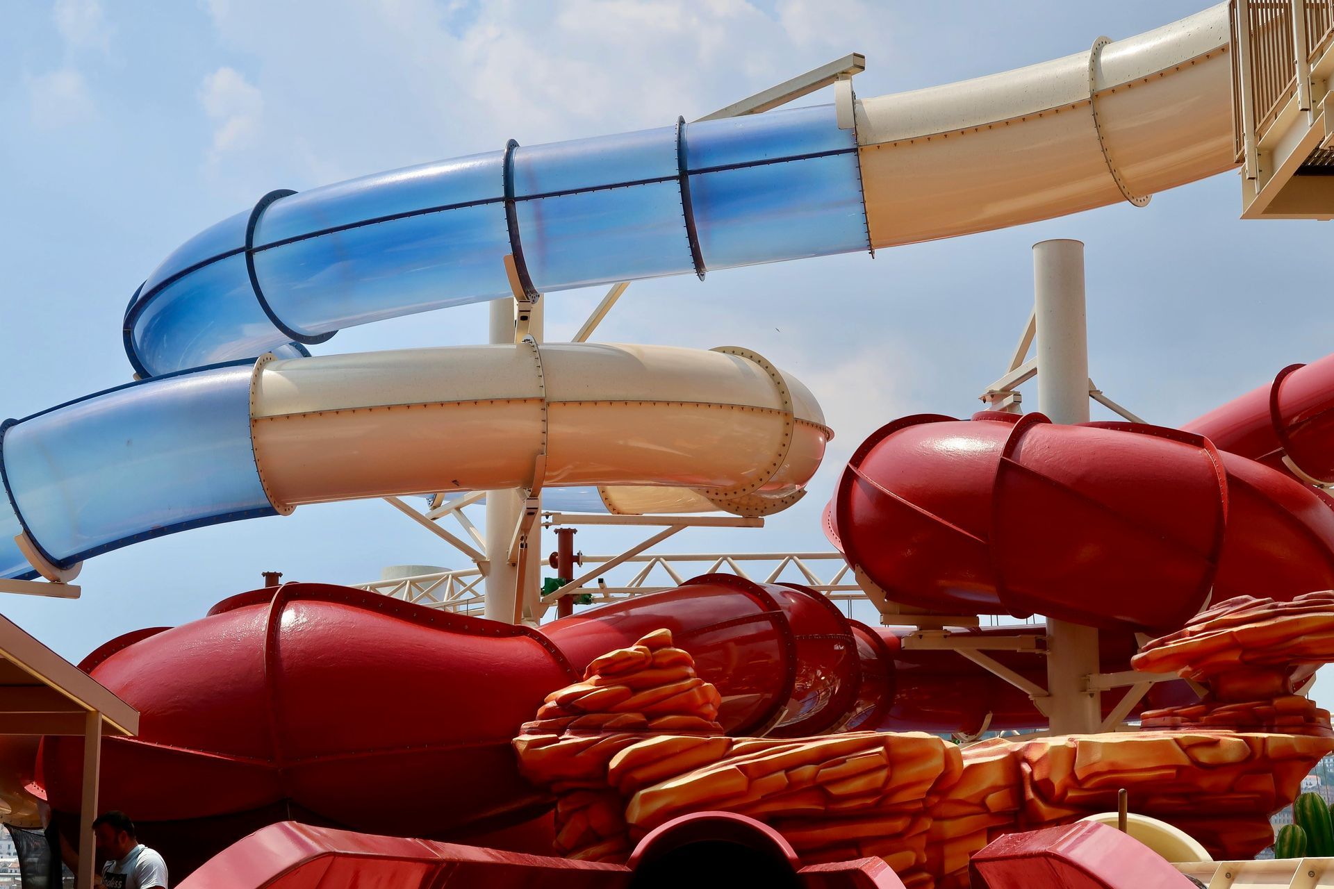 Water slides at a water park with blue, tan, and red tubes on a sunny day.