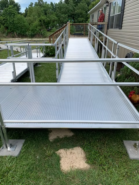 Aluminum ramp with railings leads from ground to a house deck.  Green grass surrounds it.