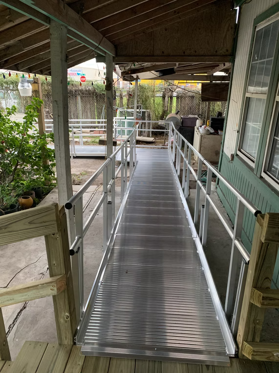 Aluminum ramp with handrails leading to a building's entrance. The ramp is on a porch.