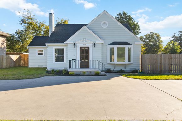 Light blue house with a black roof and a paved driveway.