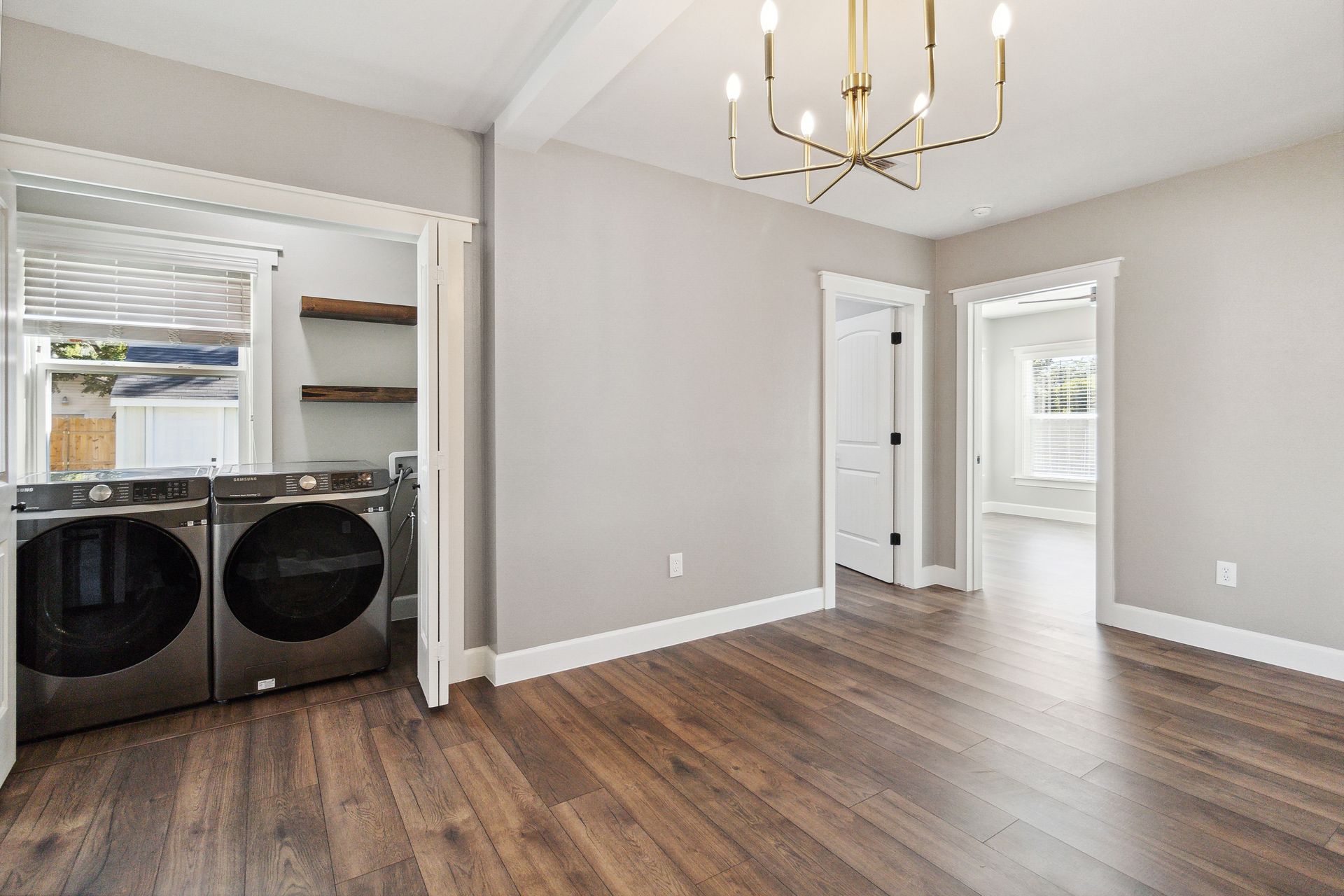 Laundry room with washer, dryer, wooden floor, gray walls, and a chandelier.