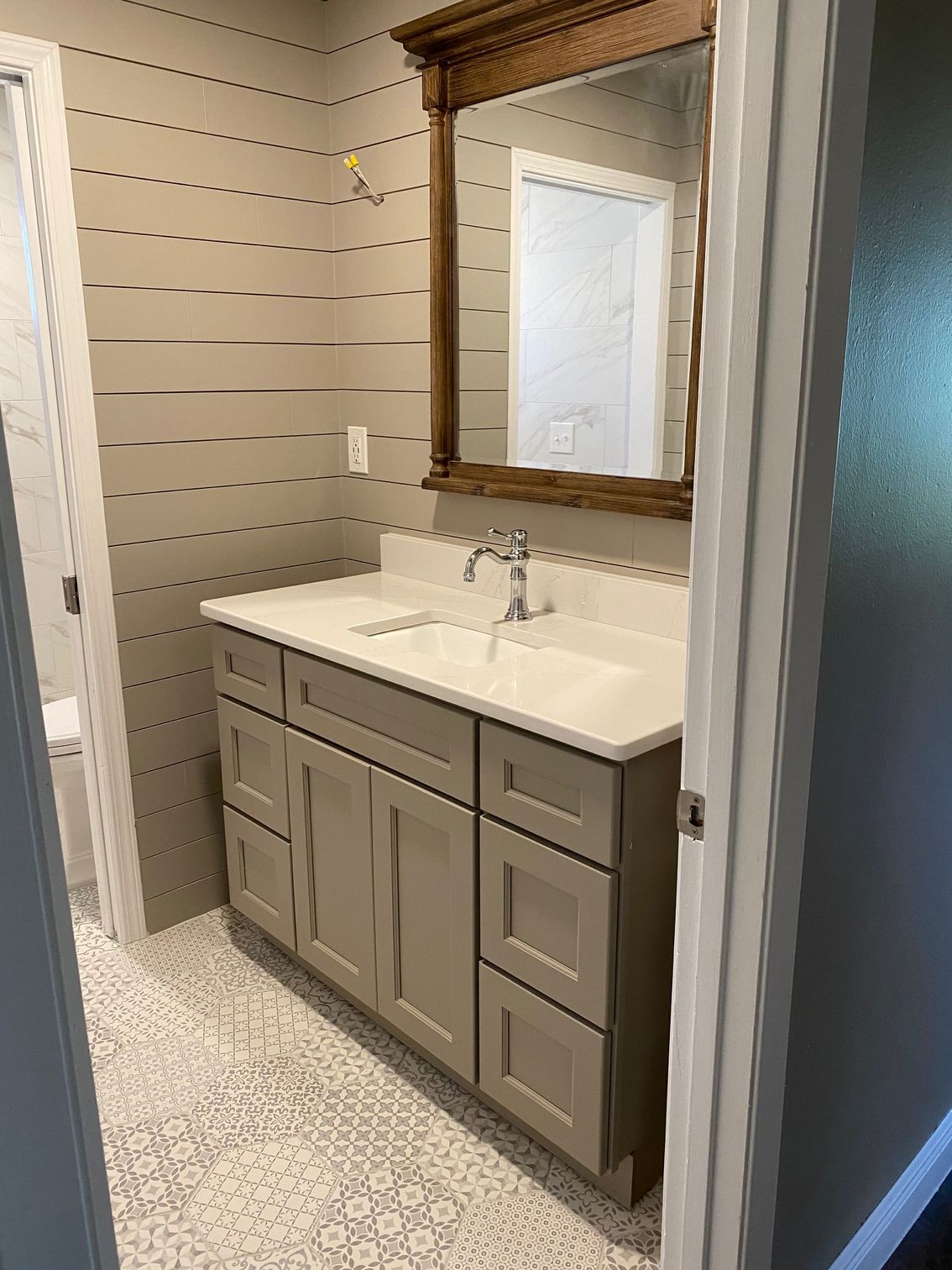 Bathroom with a beige vanity, white countertop, and brown framed mirror. Gray and white patterned floor.