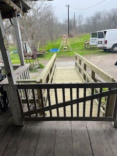 Wooden bridge with handrails leads to a path through a grassy area; a white van is parked nearby.