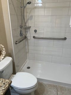 Bathroom with a white tiled shower, grab bars, and a toilet.