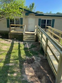 Ramp and steps lead to a beige house with green shutters and a door, set on grass.