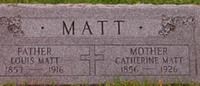 A grave marker for Louis Matt (1857–1916) and Catherine Matt (1856–1926) with a central cross, set on grass.