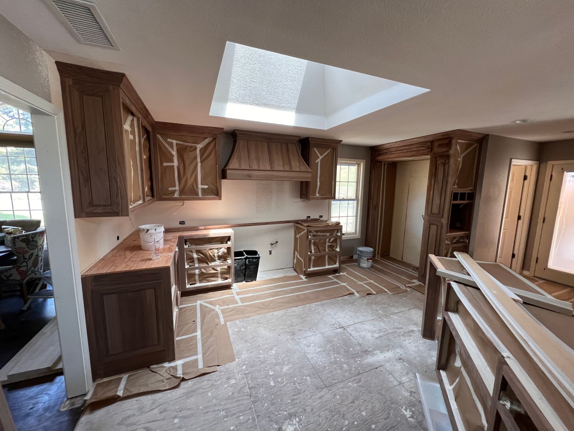 Person taping a white wall while painting, with a ladder, drop cloth, and paint supplies.