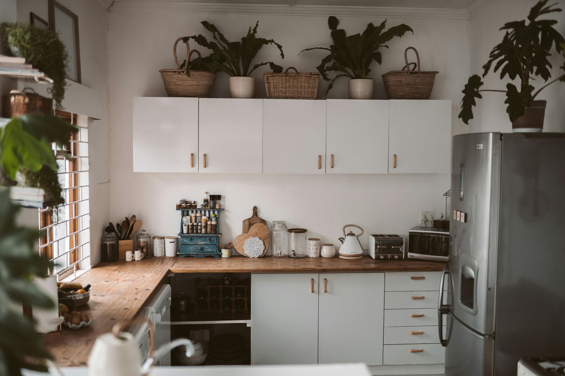 Cozy kitchen with white cabinets, wooden countertops, plants, and stainless steel refrigerator.