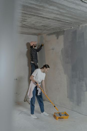 Two people painting a room. One is on a ladder, the other uses a roller.