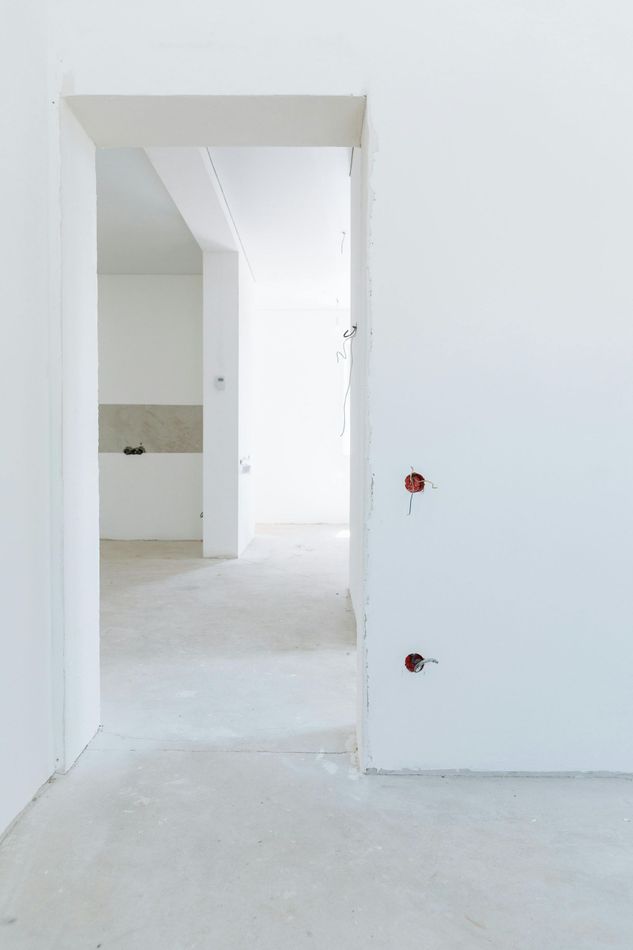 Interior of a white-walled room, concrete floor, open doorway leading to another room, unfinished construction.