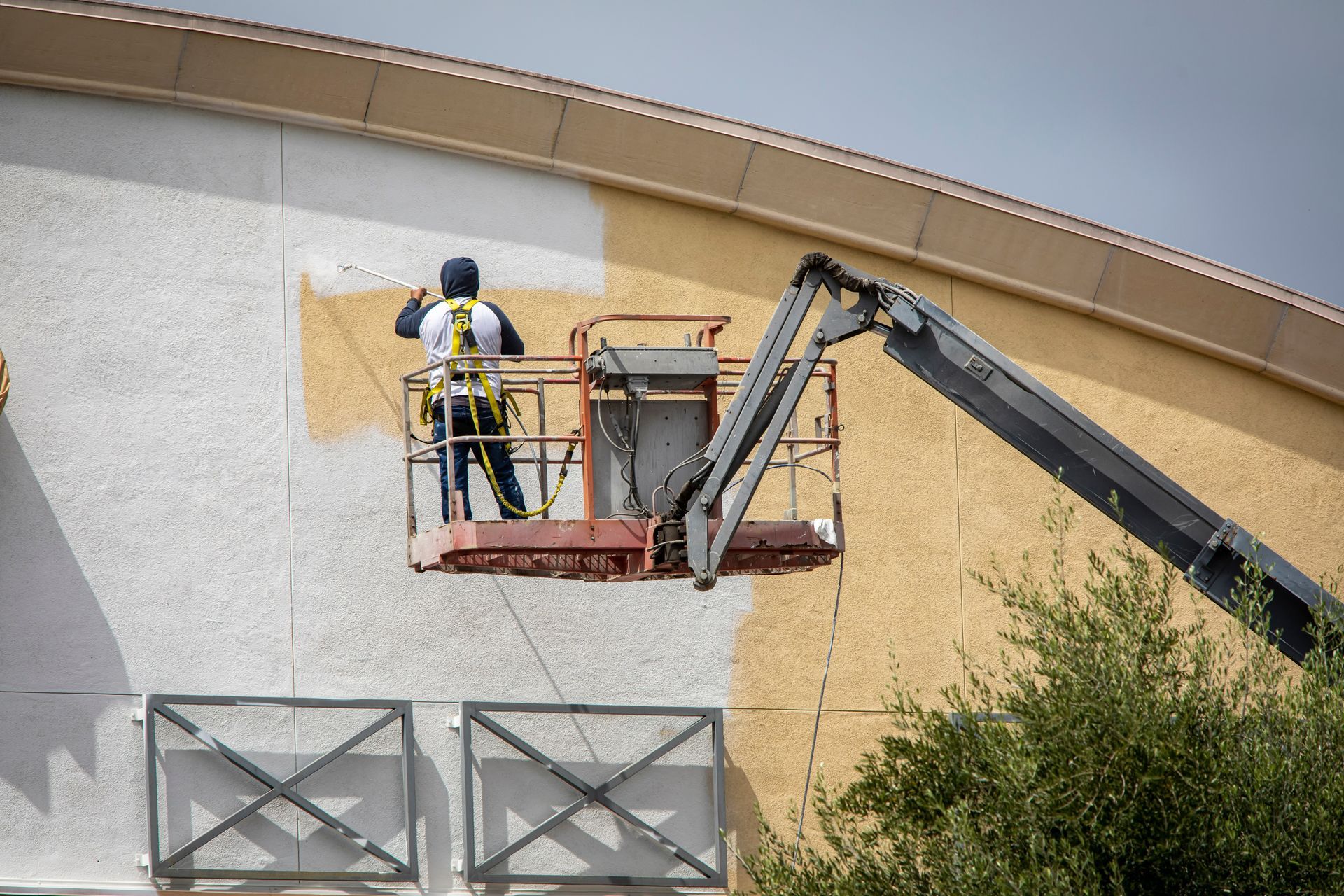 A person painting the exterior of a building from a lift, against a beige and white background.