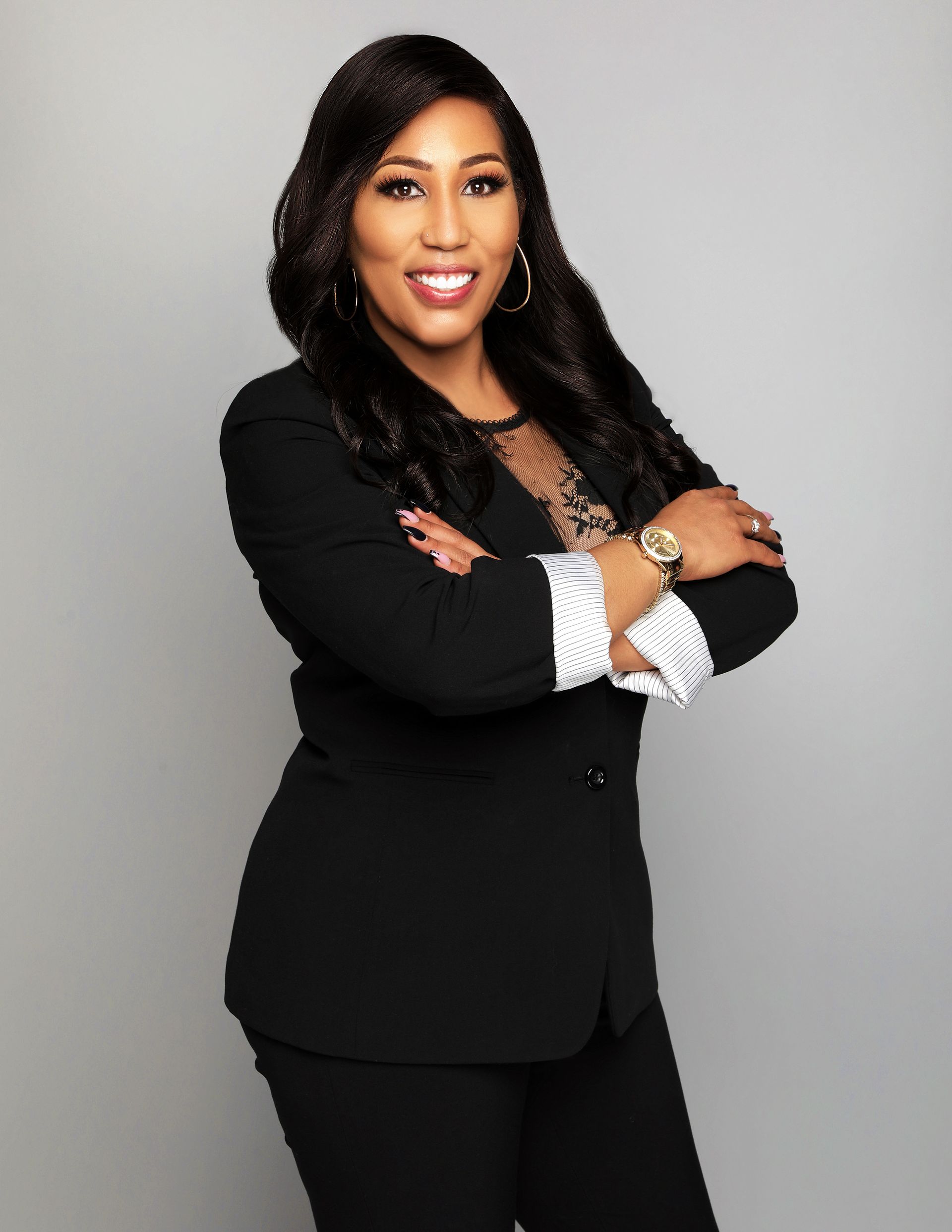 Woman in black blazer with arms crossed, smiling.