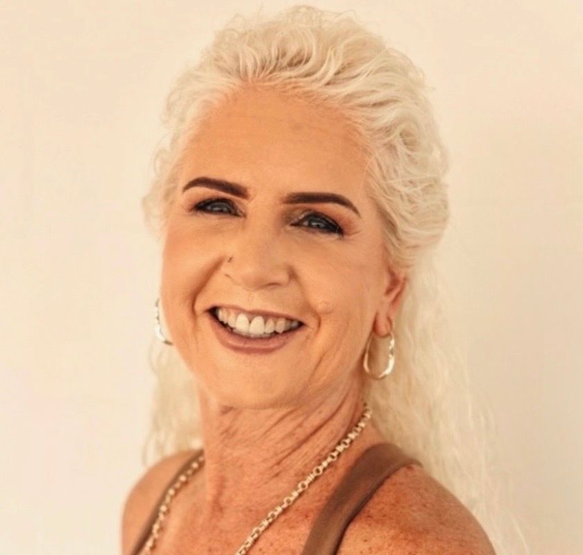 Woman with gold makeup and shimmering background, finger on lip.