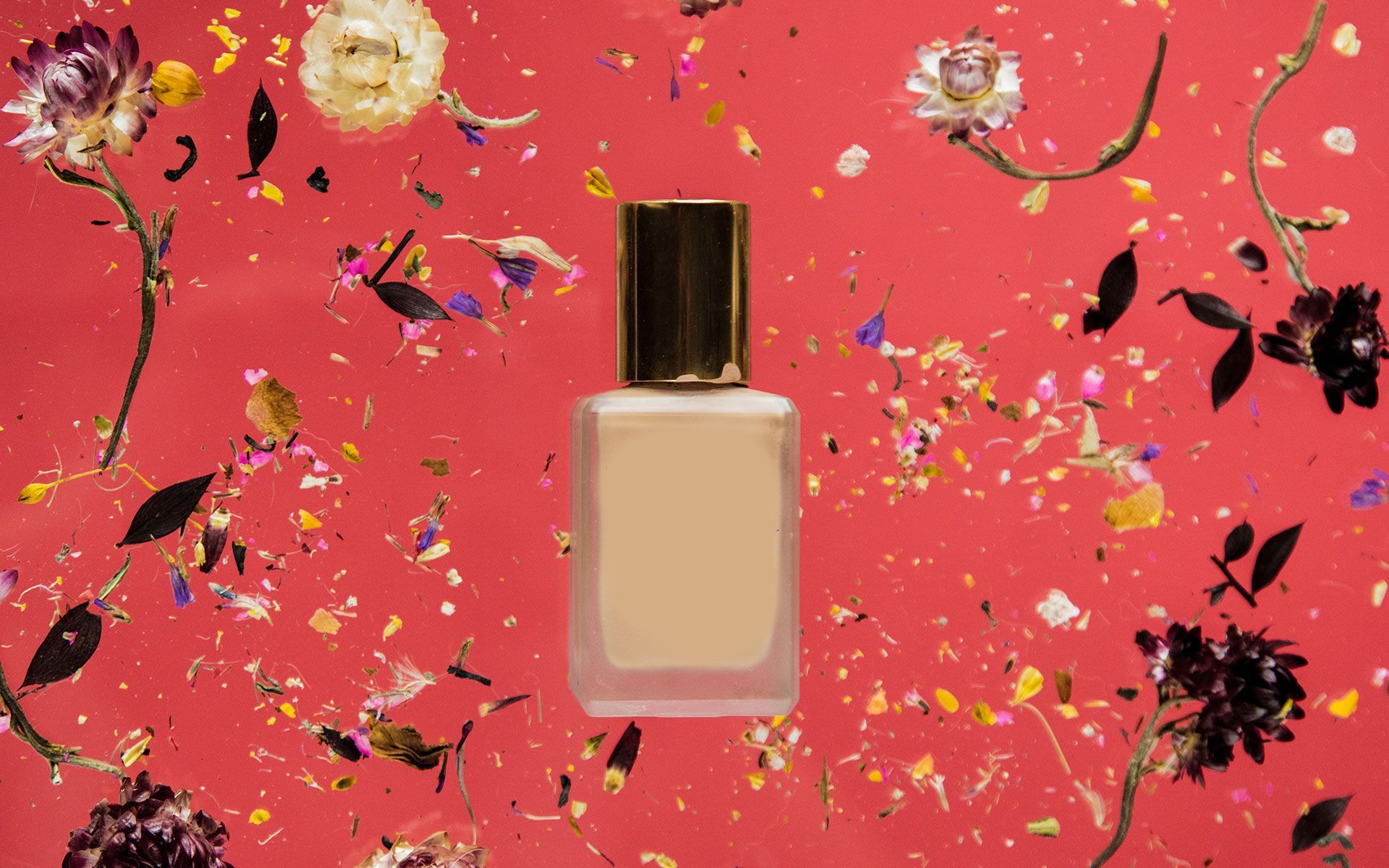 Square perfume bottle with a gold cap on a red background with scattered flowers.