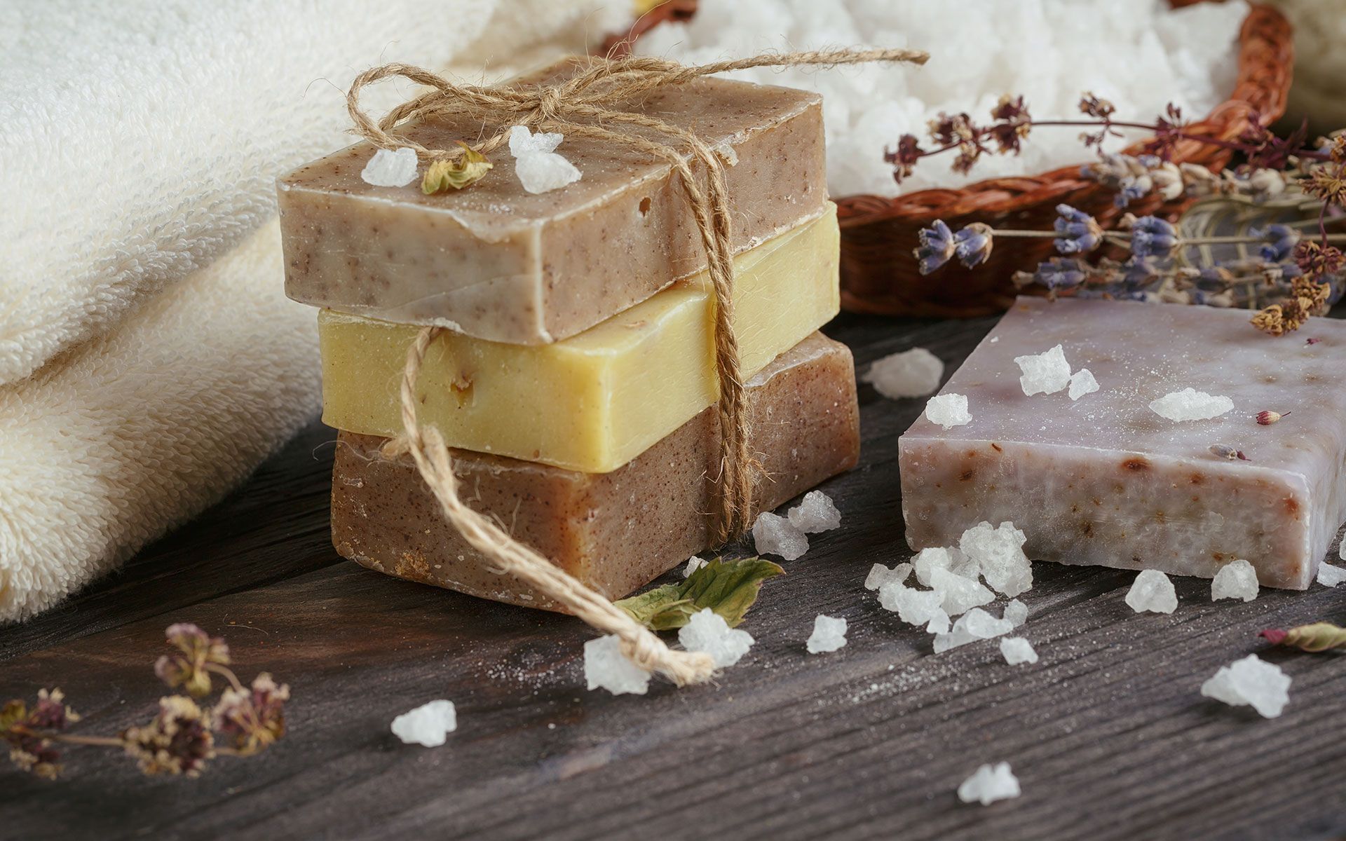 Stack of three soaps tied with twine, next to a soap, towels, and salt on a wooden surface.