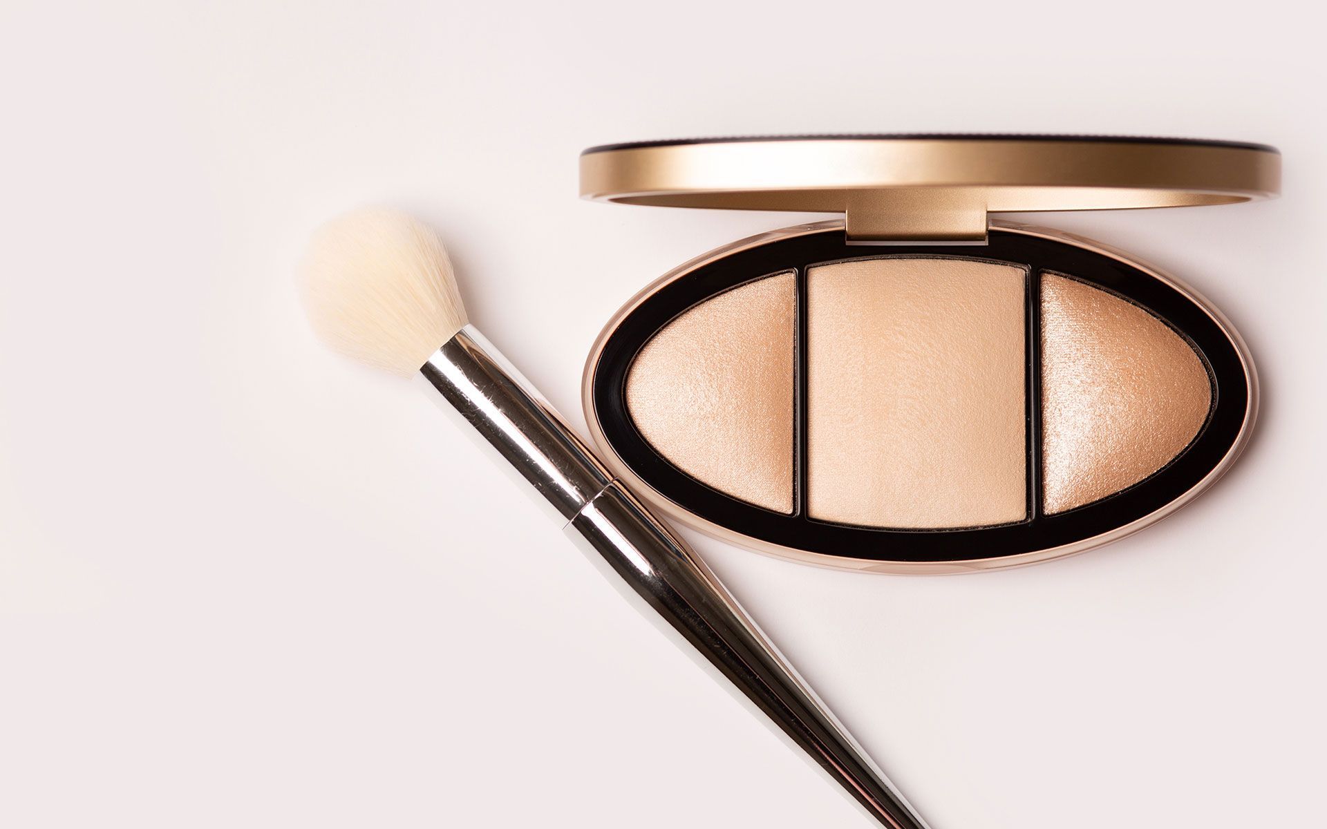 Cosmetic highlighter palette with a brush, gold and beige.