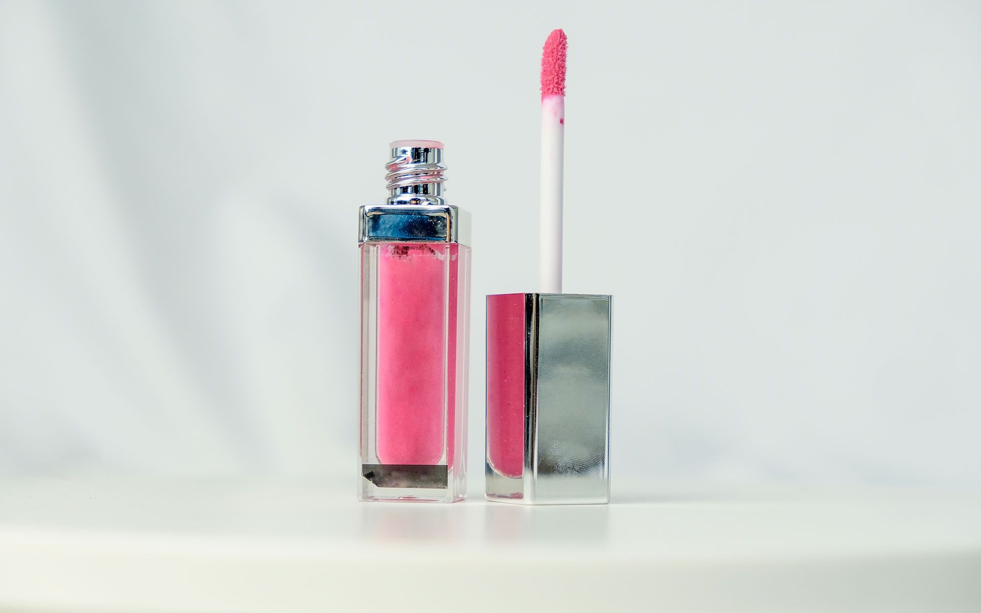 Pink lip gloss bottle, with applicator, on white surface.