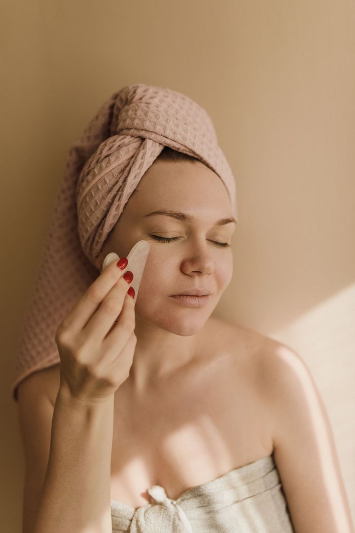 Person applying skincare with a cotton pad, wearing a towel turban in warm indoor light