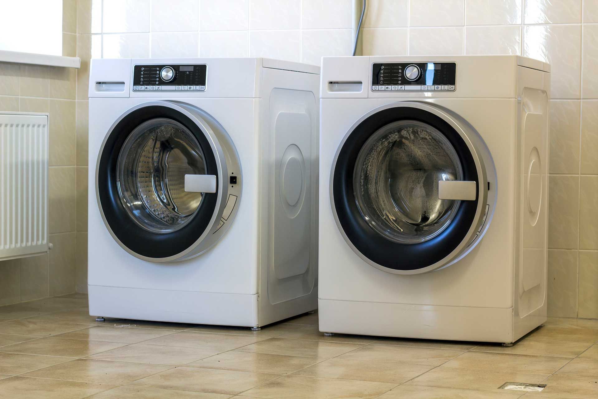 Two white washing machines are sitting next to each other in a laundry room.