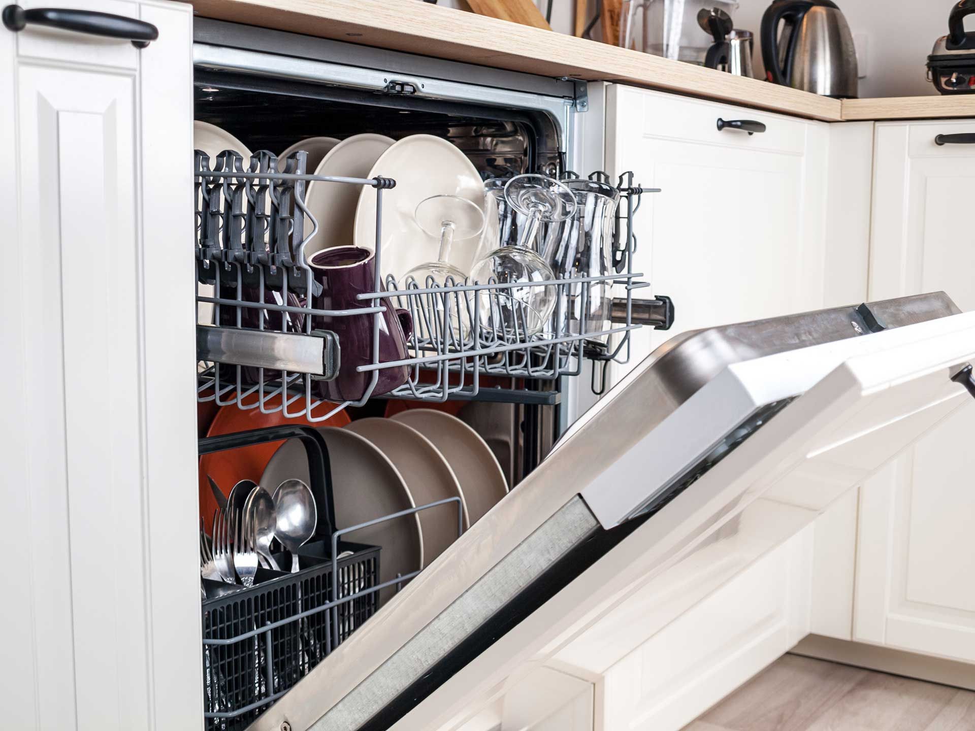 A dishwasher is filled with dishes and glasses in a kitchen.