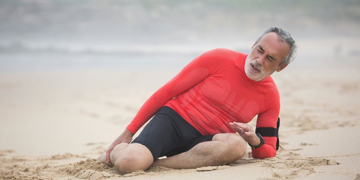 Person in red sportswear lying on a sandy beach, resting on their side.