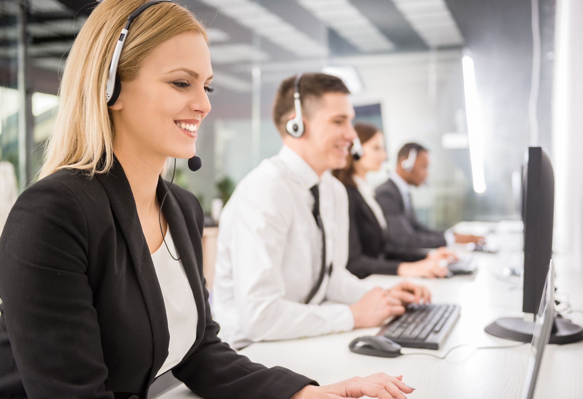A woman wearing a headset is sitting in front of a computer in a call center.
