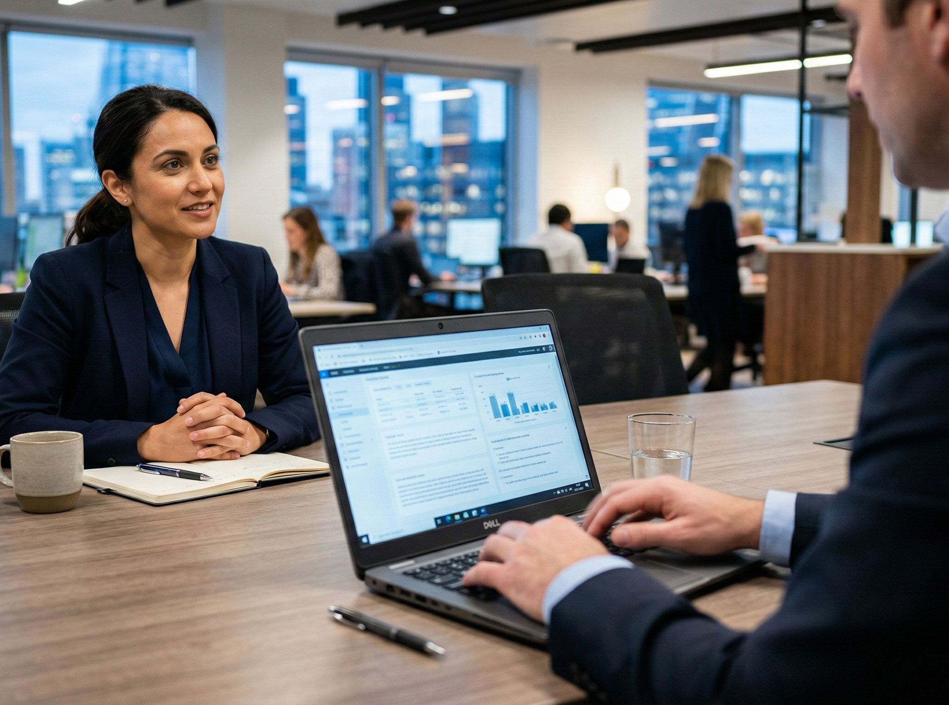 Woman and man in a business meeting, looking at a laptop with data charts in an office setting.