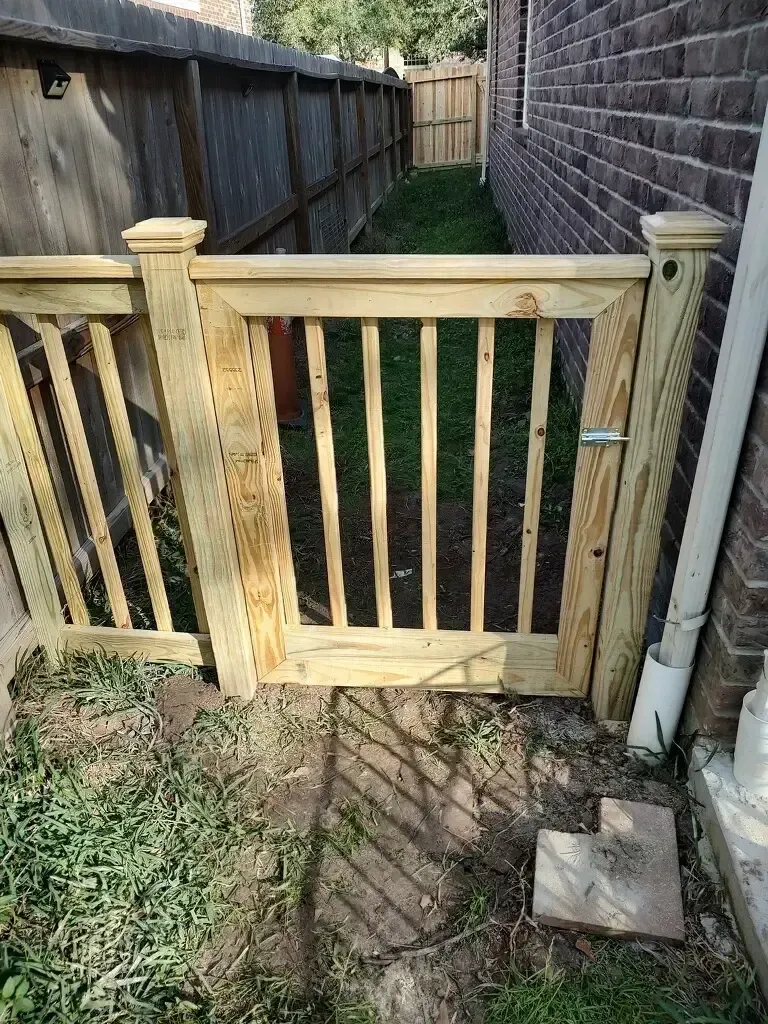 A wooden gate is sitting next to a brick fence.