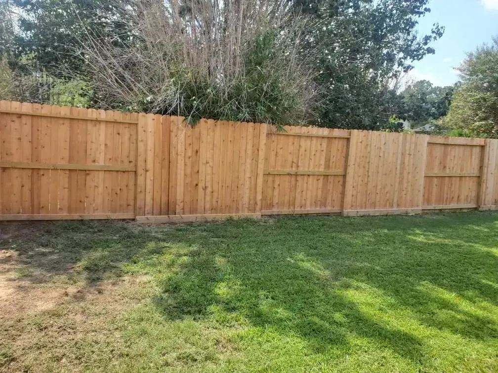 A wooden fence is in the middle of a lush green yard.