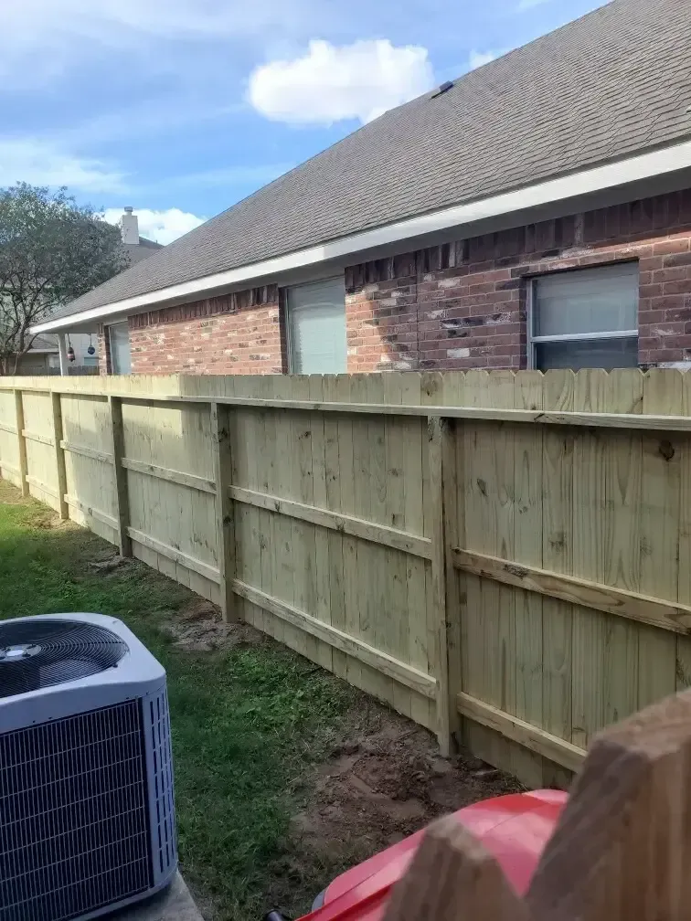 A wooden fence is sitting in front of a brick house.