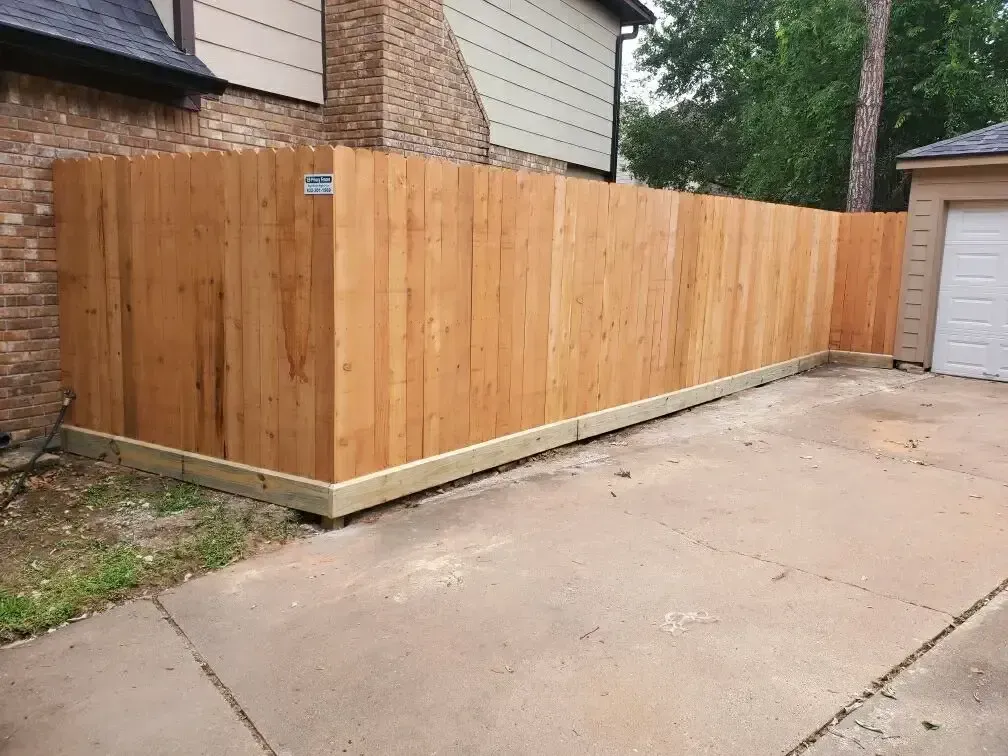 A wooden fence is sitting on the side of a driveway next to a garage.